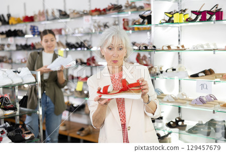 Mature woman who came to shoe store for shopping, chooses summer shoes 129457679
