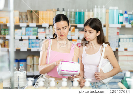 Positive mother and daughter standing at pharmacy or department of household chemicals, choosing feminine pads 129457684