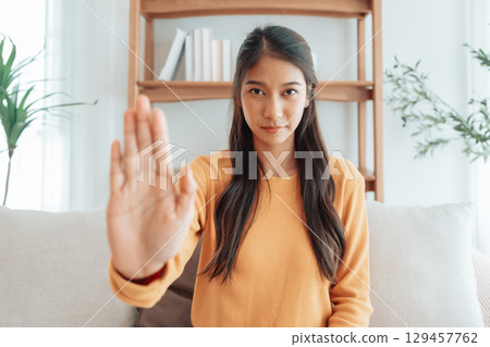 Young Asian woman with serious expression raising her hand stop gesture Young Asian woman with serious expression raising her hand stop gesture 129457762
