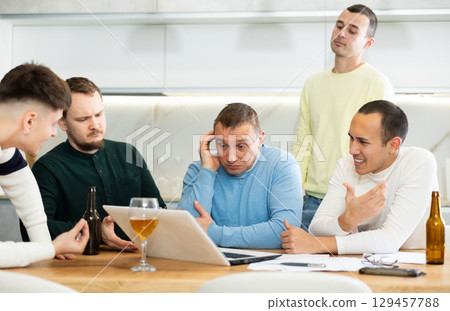 Worried male friends trying to solve problem together on laptop 129457788