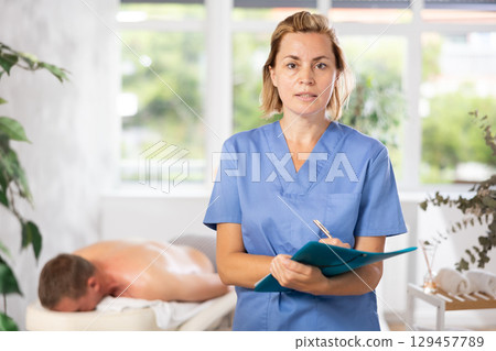 Woman physiotherapist writes down and enters patients data into medical card. 129457789