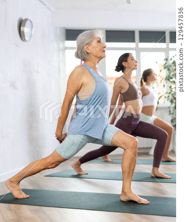 Senior woman doing Virabhadrasana during yoga training in fitness studio Senior woman doing Virabhadrasana during yoga training in fitness studio 129457836