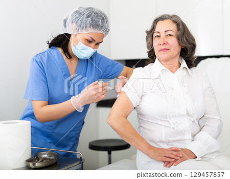 Nurse in protective mask making injection of vaccine to woman Nurse in protective mask making injection of vaccine to woman 129457857