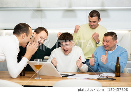 Group of friends watching football match on a laptop together and drinking beer Group of friends watching football match on a laptop together and drinking beer 129457898