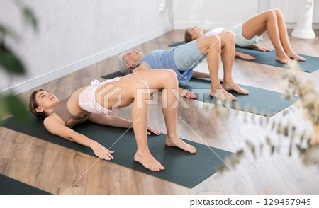Mom, grandma and teen daughter do half bridge Setu Bandha Sarvangasana, glute bridge pose Mom, grandma and teen daughter do half bridge Setu Bandha Sarvangasana, glute bridge pose 129457945
