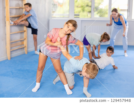 Children practicing in pair self-defence movements with female trainer supervision Children practicing in pair self-defence movements with female trainer supervision 129457948