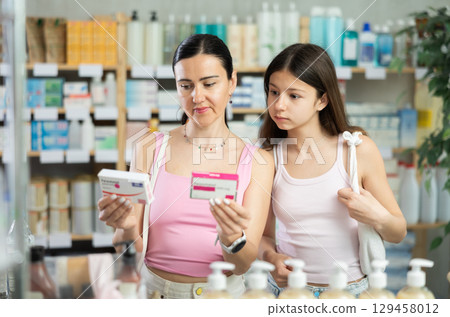 Attentive interested mother and daughter clients choosing between two boxes of paracetamol antipyretic pills in drug store. Family in pharmacy 129458012