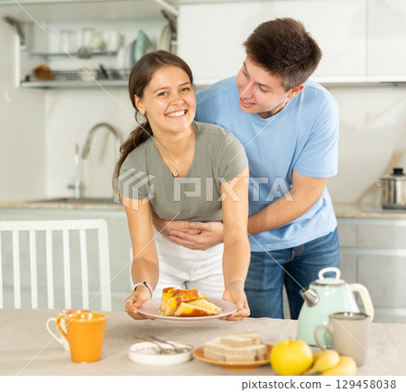 Cheerful young couple serving table for tea-time at home kitchen Cheerful young couple serving table for tea-time at home kitchen 129458038