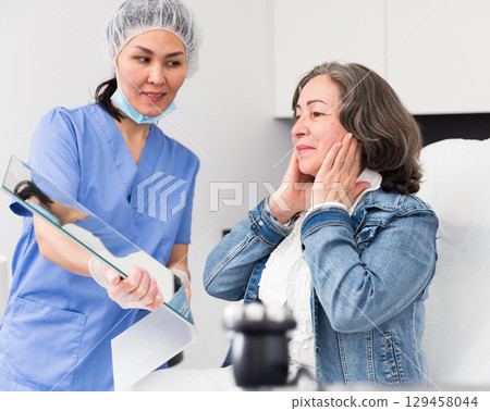 Smiling mature female patient satisfied with received cosmetological procedure in clinic 129458044
