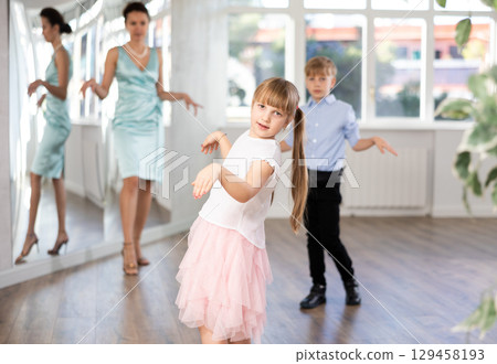 Girl rehearsing elegant curtsy with boy dance partner and female teacher 129458193