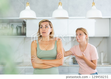 Agitated daughter imploringly asks angry mother for forgiveness. 129458231