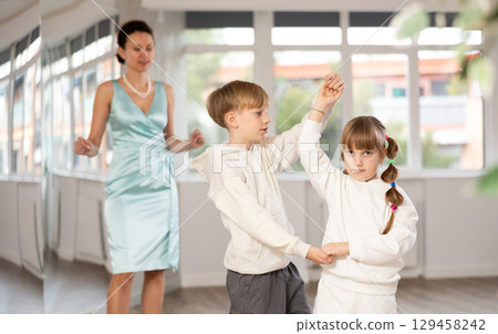 Tween girl and boy practicing waltz in dance hall with female mentor 129458242