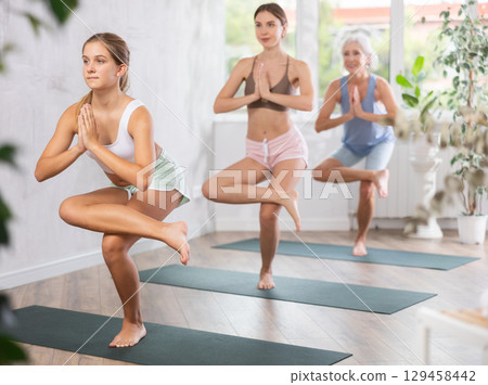 Fitness, sport and healthy lifestyle concept: woman different ages doing yoga pose - vrikshasana pose on mat in studio Fitness, sport and healthy lifestyle concept: woman different ages doing yoga pose - vrikshasana pose on mat in studio 129458442