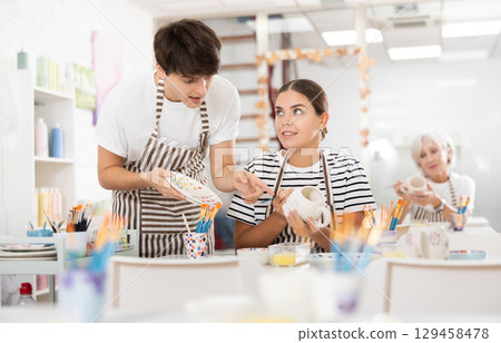 Guy assisting young girl painting ceramic mugs in pottery class Guy assisting young girl painting ceramic mugs in pottery class 129458478