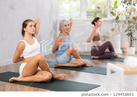 Three generations of women perform sitting Gomukhasana cows head in gym Three generations of women perform sitting Gomukhasana cows head in gym 129458601