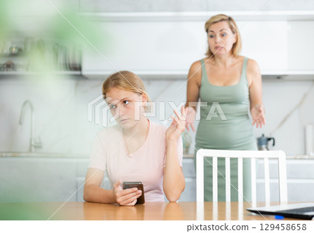 Teenage girl with smartphone making dismissive gesture to mother Teenage girl with smartphone making dismissive gesture to mother 129458658