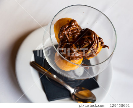 Portion of three profiteroles with melted chocolate 129458691