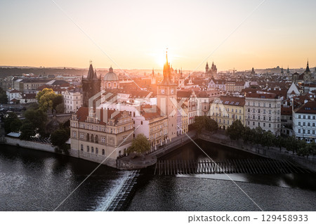 The early morning light casts a golden hue over the Old Town of Prague, highlighting the historic architecture and the serene Vltava River. This aerial view showcases a breathtaking cityscape. 129458933