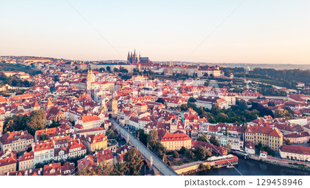 A breathtaking view of Prague at sunrise reveals the city's iconic skyline. The Vltava river gracefully flows alongside historic buildings, with the Charles Bridge and castle in the background. 129458946