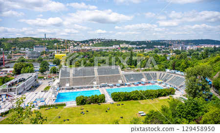 People relax and swim at Podoli Swimming Pool in Prague on a warm summer day. The vibrant atmosphere reflects the joys of summer in Czechia. A beautiful location for leisure and fun. People relax and swim at Podoli Swimming Pool in Prague on a warm summer day. The vibrant atmosphere reflects the joys of summer in Czechia. A beautiful location for leisure and fun. 129458950
