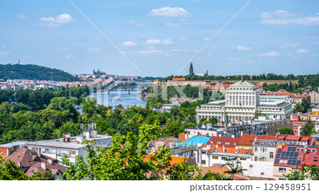 The stunning panorama of Prague showcases the Vltava River flowing through the city. Lush greenery and historical landmarks create an inviting atmosphere on a clear day. 129458951