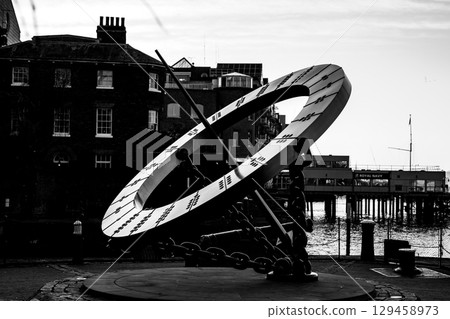A large sundial stands prominently near Tower Bridge in London. The sun casts shadows on its engraved markings, offering a unique timekeeping experience against a historical backdrop. 129458973