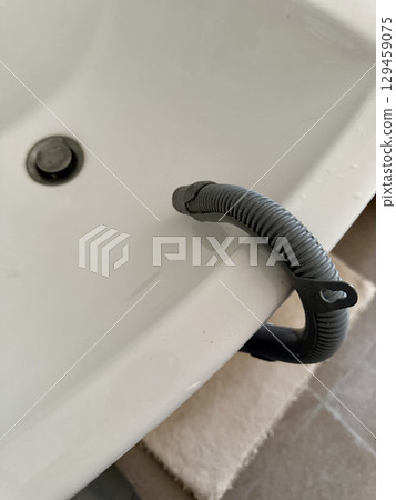 Macro view of a gray flexible drain tube leading to a white ceramic sink, a way of using washing machine without water drainage.jpg 129459075