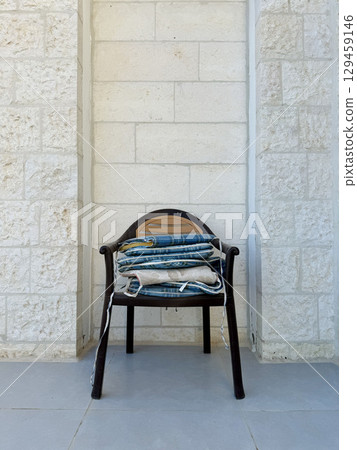Black plastic chair with neatly stacked blue patterned cushions on tiled patio, highlighting outdoor furniture, comfort, and casual home garden decor. 129459146