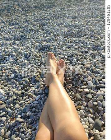 Woman with tanned skin in a relaxed mood resting her bare legs on a sunny beach, representing a summer holiday and self-care Woman with tanned skin in a relaxed mood resting her bare legs on a sunny beach, representing a summer holiday and self-care 129461285