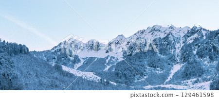 Snow-covered mountain range under a clear blue sky, showcasing rugged peaks and serene winter landscape, outdoor adventure and exploration in nature's beauty, natural background 129461598