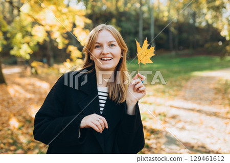 Portrait of pretty young 30s woman in evening autumn sun, smiling. Autumn landscape, calmness, tranquility concept. Pretty female holding leaf on nature background. High quality photo. Portrait of pretty young 30s woman in evening autumn sun, smiling. Autumn landscape, calmness, tranquility concept. Pretty female holding leaf on nature background. High quality photo. 129461612