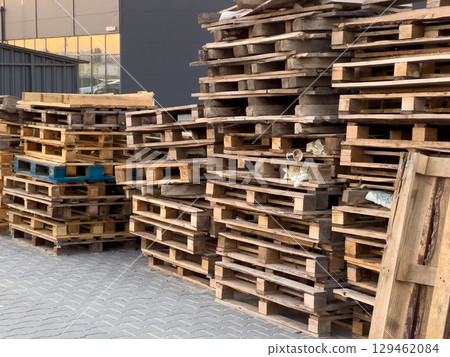 Stacked wooden pallets are organized in a commercial yard as sunlight casts warm hues over the scene, highlighting their weathered textures 129462084