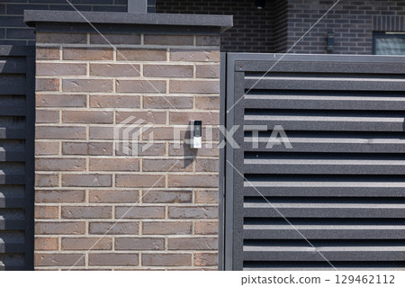 Modern intercom system mounted on a brick wall next to a slatted fence creates a welcoming home entrance during the day Modern intercom system mounted on a brick wall next to a slatted fence creates a welcoming home entrance during the day 129462112