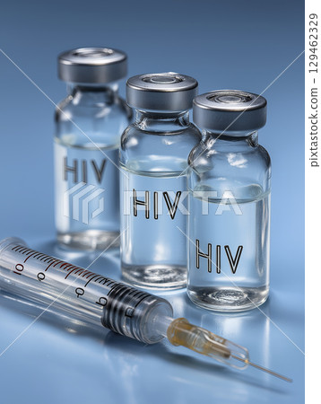 Transparent glass medical vials labeled HIV stand beside clear plastic syringe reflective blue surface, conveying critical nature of medical treatment, research, and hopeful pursuit of cure 129462329