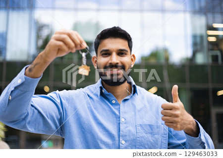 A smiling man holds up house keys, giving a thumbs up with a building in the background. A smiling man holds up house keys, giving a thumbs up with a building in the background. 129463033