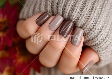 Woman showing brown ombre fall manicure holding knitted sweater 129463293