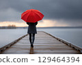 Moody Sky And Vibrant Umbrella Solitary Figure On A Wet Wooden Pier, Dark Coat Composition 129464394