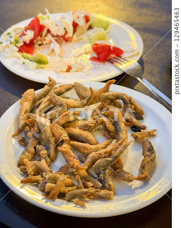 Fried Fish and Partially Eaten Salad. Close-up of crispy fried fish with partially eaten salad on table under warm sunset light. Concept of casual dining, comfort food, relaxed evening meal 129465463