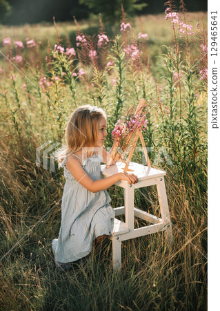 Young girl painting flowers in a meadow surrounded by tall grass during golden hour Young girl painting flowers in a meadow surrounded by tall grass during golden hour 129465641