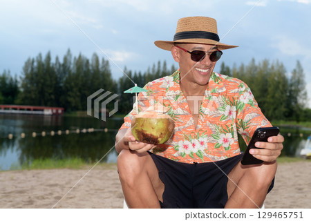 Man tourist sitting on beach using mobile phone and holding coconut water Man tourist sitting on beach using mobile phone and holding coconut water 129465751