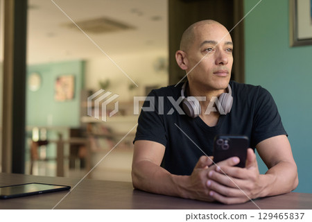 Hispanic bald man in library wearing black t-shirt and headphones looking through window indoors 129465837
