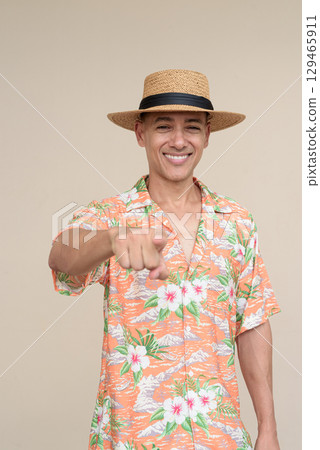 Smiling Hispanic Tourist Man Wearing Panama Hat and Tropical Hawaiian Shirt Pointing Finger 129465911