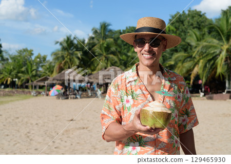 Hispanic Male Tourist in Panama Hat and Tropical Shirt Summer Vacation at Beach Holding Coconut 129465930