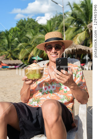 Hispanic man tourist sitting and using phone while having coconut water drink 129465946