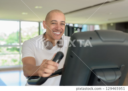 Latin man cycling on stationary exercise bike in gym, training, wellness and healthy lifestyle 129465951
