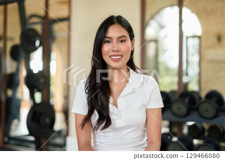 Young Asian woman in polo shirt at gym using phone in modern indoor training location 129466080