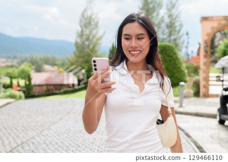 Asian woman using phone in white polo shirt on European style city street during summer Asian woman using phone in white polo shirt on European style city street during summer 129466110