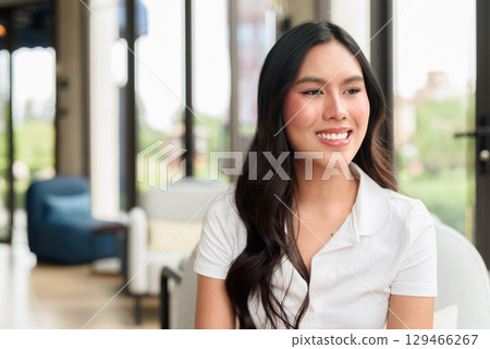 Young Asian woman in white polo shirt indoors, hotel lounge or cafe interior, tourist portrait Young Asian woman in white polo shirt indoors, hotel lounge or cafe interior, tourist portrait 129466267