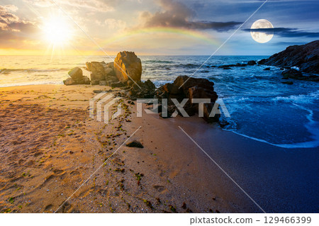 landscape by the sea in summer. day and night time change concept. beautiful beach with rocks washed by calm waves with sun and moon at twilight. view to horizon under blue sky with clouds landscape by the sea in summer. day and night time change concept. beautiful beach with rocks washed by calm waves with sun and moon at twilight. view to horizon under blue sky with clouds 129466399