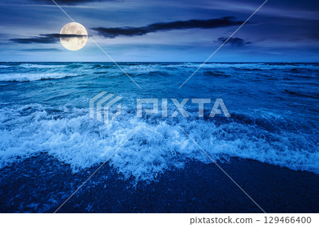 sea tide before storm at night. wave splash with foam on wet sandy beach in full moon light. windy weather on velvet season. dramatic seascape background sea tide before storm at night. wave splash with foam on wet sandy beach in full moon light. windy weather on velvet season. dramatic seascape background 129466400